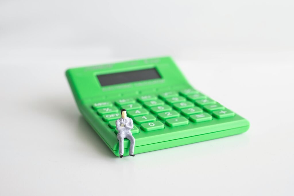 Conceptual image of a miniature businessman sitting on a green calculator, symbolizing finance and calculation.