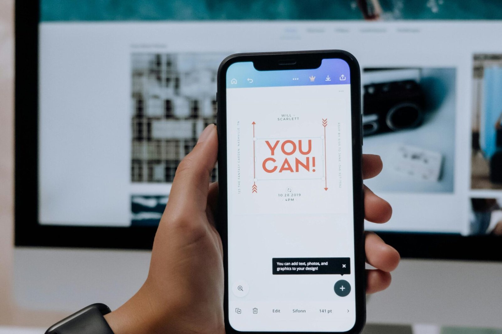 Hand holding smartphone with 'You Can!' message in front of desktop screen.