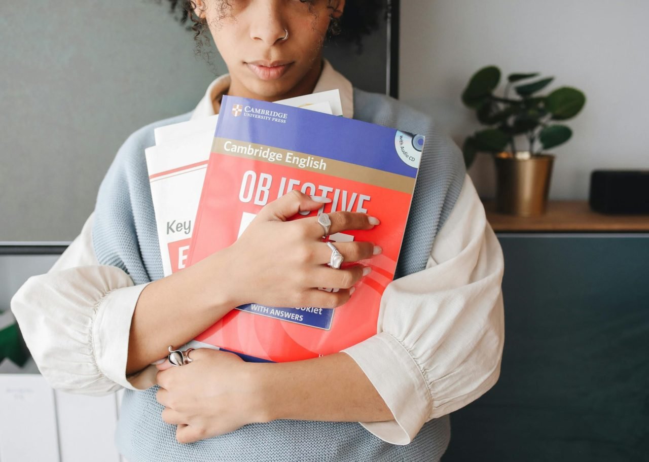 Young woman holding language study books indoors, symbolizing education and learning.
